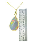 Opal pendant on a gold chain with a ruler for scale on a white background