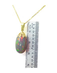 Opal pendant necklace with gold chain on a white background, accompanied by a ruler for scale.