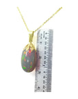 Ethiopian Welo opal pendant with vibrant red fire in 14k yellow gold, shown with a ruler.