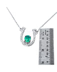 Horseshoe-shaped pendant with natural emerald gemstone and diamonds next to a ruler for scale on a white background