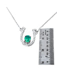 14K white gold horseshoe necklace with oval emerald and diamond accents, shown with ruler for size.