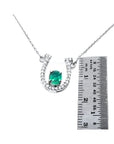 14K white gold horseshoe necklace with oval emerald and diamond accents, shown with ruler for size.