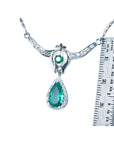 White gold emerald necklace with a green teardrop pendant next to a ruler for scale on a white background