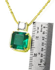 18k yellow gold necklace with an Asscher cut emerald gemstone pendant next to a ruler for scale on a white background