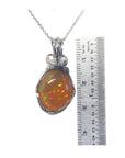 Opal pendant on a silver chain with a ruler for scale on a white background