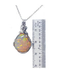 5.96 ct. Welo Ethiopian multicolor opal pendant with silver wire wrap setting, next to a ruler.