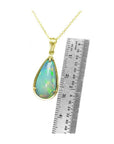 Pear-shaped Ethiopian opal pendant with blue-violet play-of-color in 14K yellow gold, shown with ruler.