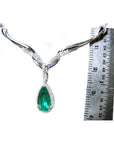 White gold necklace with a pear cut emerald gemstone in a halo diamond next to a ruler on a white background