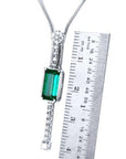 Necklace with a natural emerald gemstone and white gold chain next to a ruler for scale on a white background