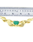 Emerald Claddagh necklace, heart-cut deep green emerald in 14K yellow gold, held by hands, with ruler for scale.