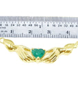 Emerald Claddagh necklace, heart-cut deep green emerald in 14K yellow gold, held by hands, with ruler for scale.