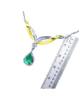 Jewelry with a teardrop natural emerald gemstone and gold accents next to a ruler for measuring size on a white background