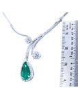 White gold necklace with a teardrop emerald gemstone pendant next to a ruler for scale on a white background
