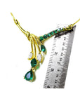 A yellow gold necklace with natural emeralds and diamonds gemstones next to a ruler on a white background