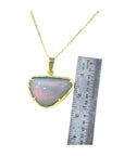 Opal pendant necklace with gold chain next to a ruler on a white background.