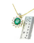 A yellow gold necklace with an oval emerald pendant next to a ruler for scale on a white background