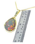 Opal pendant on a gold chain with a ruler for scale on a white background