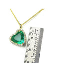 Gold necklace with a heart-shaped genuine emerald pendant next to a ruler for scale on a white background