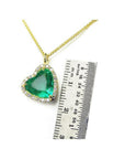 Tilted heart emerald necklace with halo diamonds on an 18K gold chain, shown with a ruler for scale.
