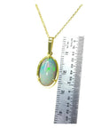 Oval Ethiopian opal pendant with bluish green hues, prong set in 14K yellow gold, shown next to a ruler.