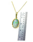 Oval Ethiopian opal pendant with bluish green hues, prong set in 14K yellow gold, shown next to a ruler.