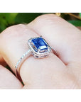 14k white gold ring with a blue natural sapphire underside view on a finger against a green leafy background