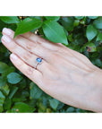 Hand wearing a 14k white gold ring with a blue natural sapphire against a green leafy background