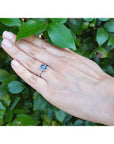 Woman's hand wearing a 1.03 ct emerald cut blue sapphire solitaire ring in 14K white gold with rope frame and accent diamonds.