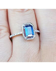 A women’s sapphire solitaire ring with a medium light blue stone, accented by diamonds, set in 14K white gold, shown on the finger.