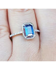 A women’s sapphire solitaire ring with a medium light blue stone, accented by diamonds, set in 14K white gold, shown on the finger.