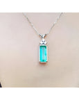 Emerald pendant with accent diamonds on a white gold chain, worn on a person's neck.