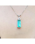 Emerald pendant with accent diamonds on a white gold chain, worn on a person's neck.