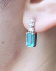 Close-up of a diamond earring with a natural emerald gemstone worn on an ear.