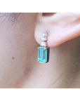 Emerald drop earring with three round diamonds in 14K white gold on an ear.