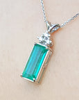 Emerald rectangular gemstone pendant with white gold chain on beige background