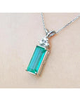 Emerald rectangular gemstone pendant with white gold chain on beige background