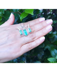 Emerald earrings and pendant set with diamonds in 14K white gold, held on a hand.