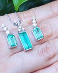 A trio set of earrings and pendant on a hand with a blurred green leaf background