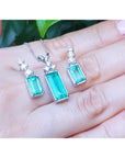 A trio set of earrings and pendant on a hand with a blurred green leaf background