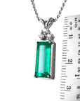 A natural emerald pendant on a chain with a ruler for scale on a white background