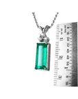 A natural emerald pendant on a chain with a ruler for scale on a white background