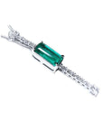 close side view of a diamond necklace with a central emerald stone on a white background