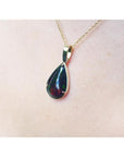 Teardrop Welo black opal pendant with red-orange and blue-green flashes on a 14K yellow gold chain.