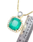 Cushion cut emerald necklace in 18K yellow gold with diamond halo, shown with a ruler for scale.