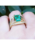 Anillo de oro con esmeralda en mano de mujer sobre un follaje verde.