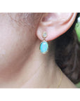 Close-up of an ear wearing a gold earring with a natural Australian opal, on a blurred background.