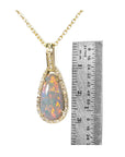 Opal pendant necklace with gold chain next to a ruler for scale on a white background