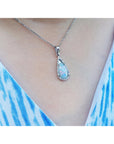 Teardrop-shaped solid opal pendant necklace on a person wearing a blue and white patterned top.
