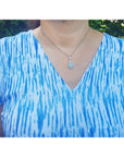 A lady wearing a blue and white tie-dye shirt with a natural opal necklace outdoors.