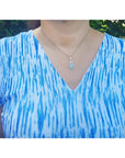Pear-shaped Australian white opal pendant in 18k white gold on a silver chain, worn on a person.